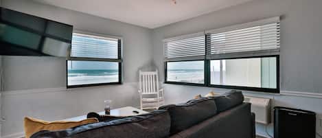 A living room with a gray sofa, a white chair, a small table with a glass, and a ceiling fan.