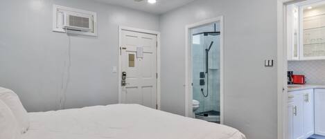 A bedroom with a bed, a ceiling fan, a white door, and a bathroom with a glass shower enclosure.