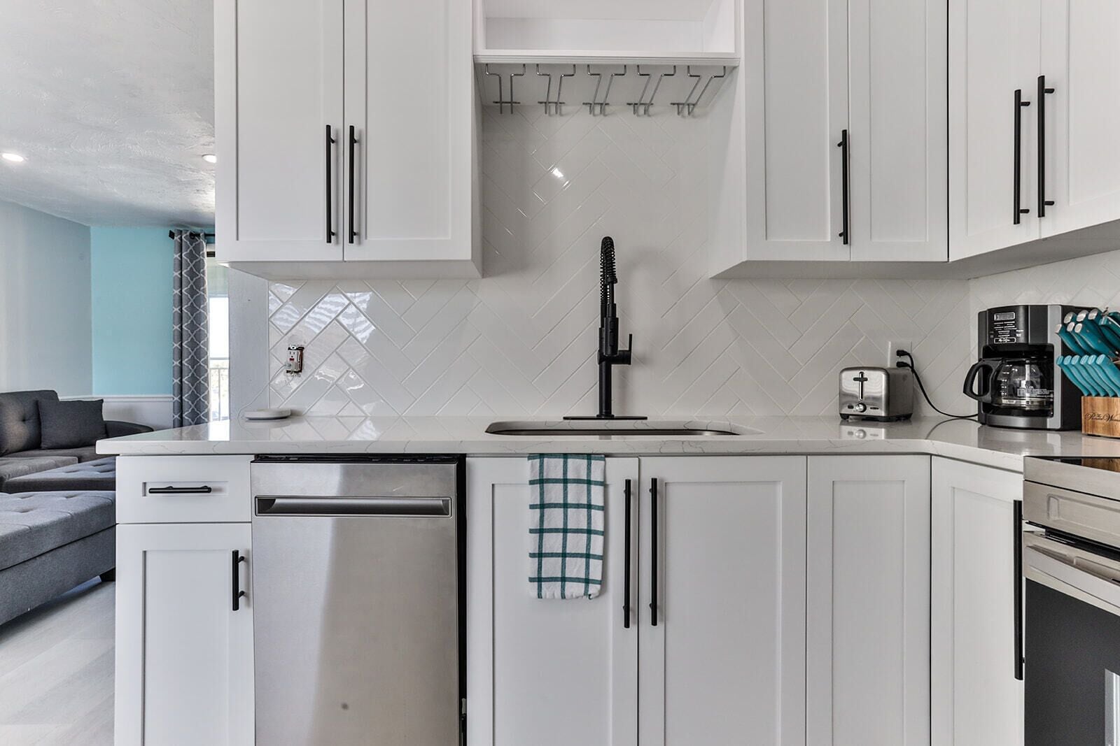 Una cocina moderna con armarios blancos, lavavajillas de acero inoxidable y cafetera.
