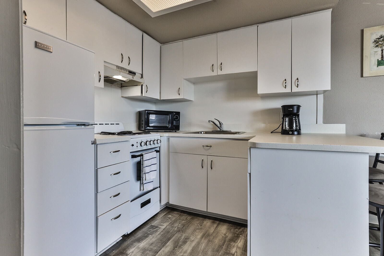 A compact kitchen with white cabinets, a built-in oven, a microwave, and a coffee maker.