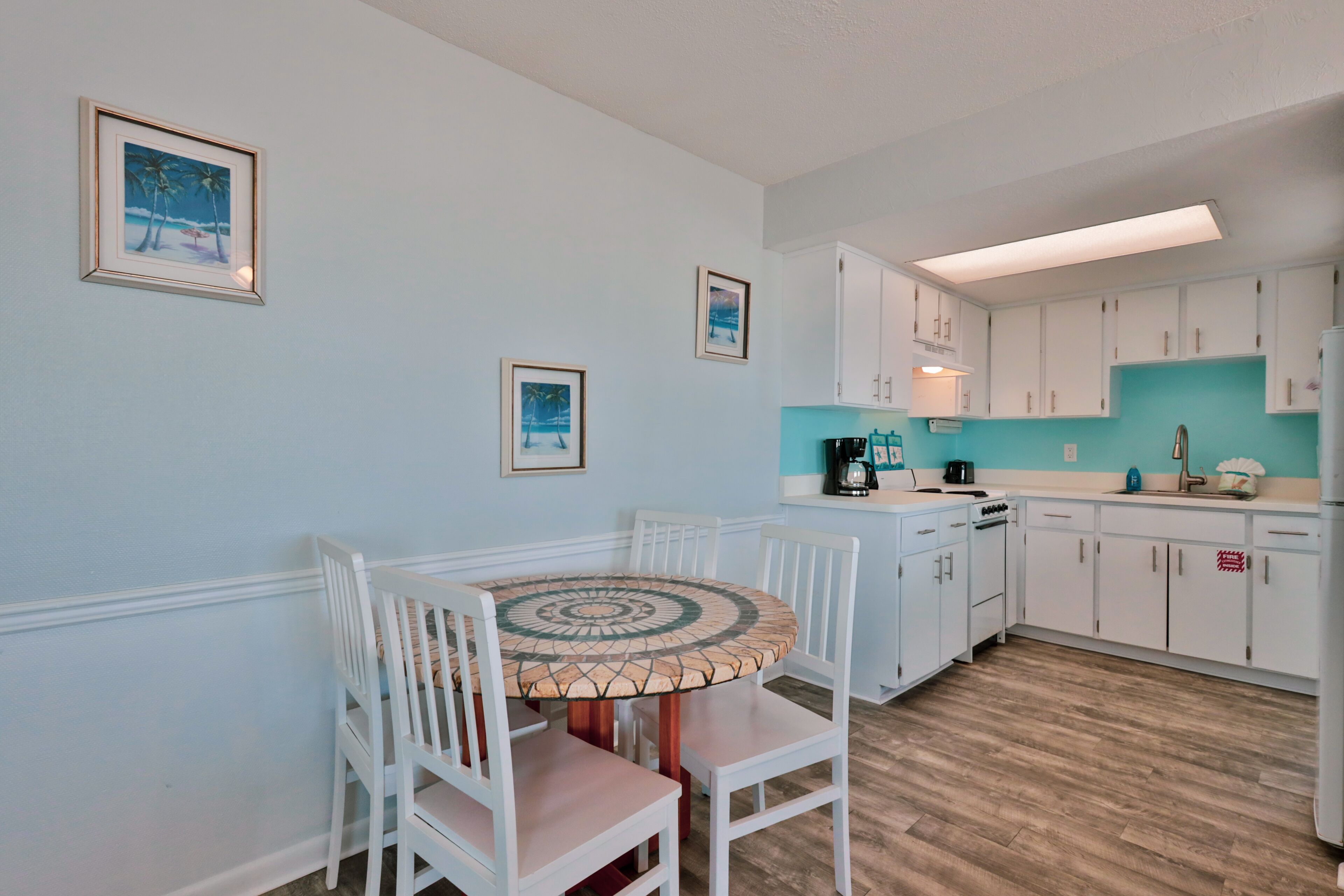 Une cuisine avec des meubles blancs, une table ronde entourée de chaises et des tableaux encadrés accrochés au mur.