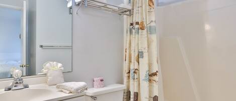Een badkamer met een witte wastafel, toilet, handdoekrek met opgevouwen handdoeken, toiletrolhouder en douchegordijn met vogelmotief.