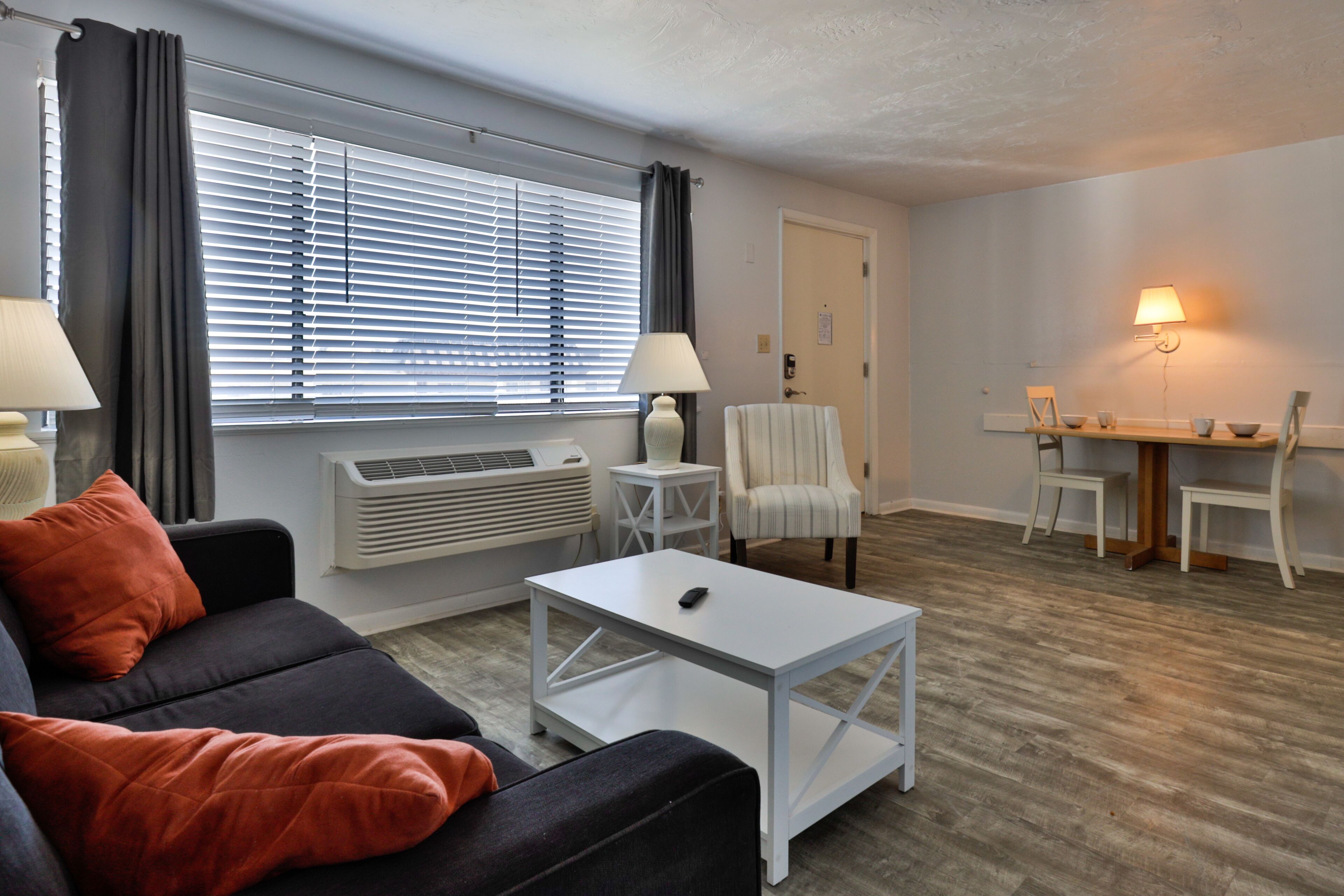 Un salon moderne comprenant un canapé, une table basse, un coin repas avec une table et des chaises, et une lampe.