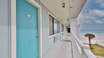 A corridor with a turquoise door, windows, and a balcony overlooking the beach.