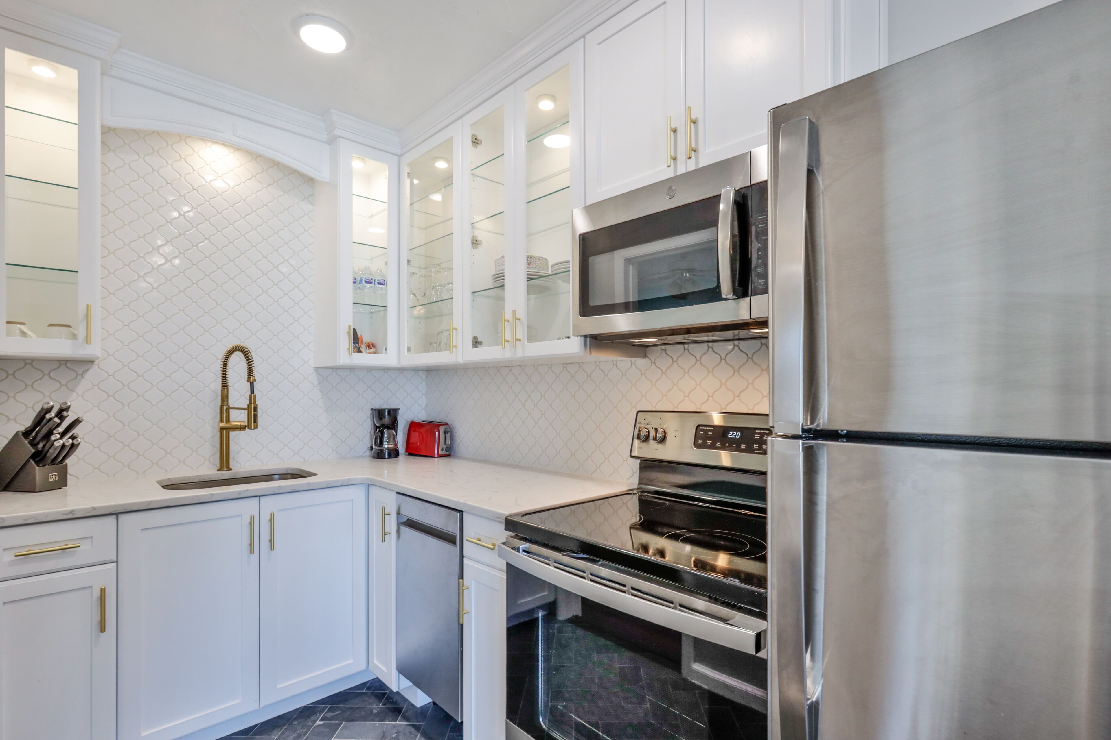 Una cocina moderna con armarios blancos, un refrigerador de acero inoxidable, un microondas y un horno.