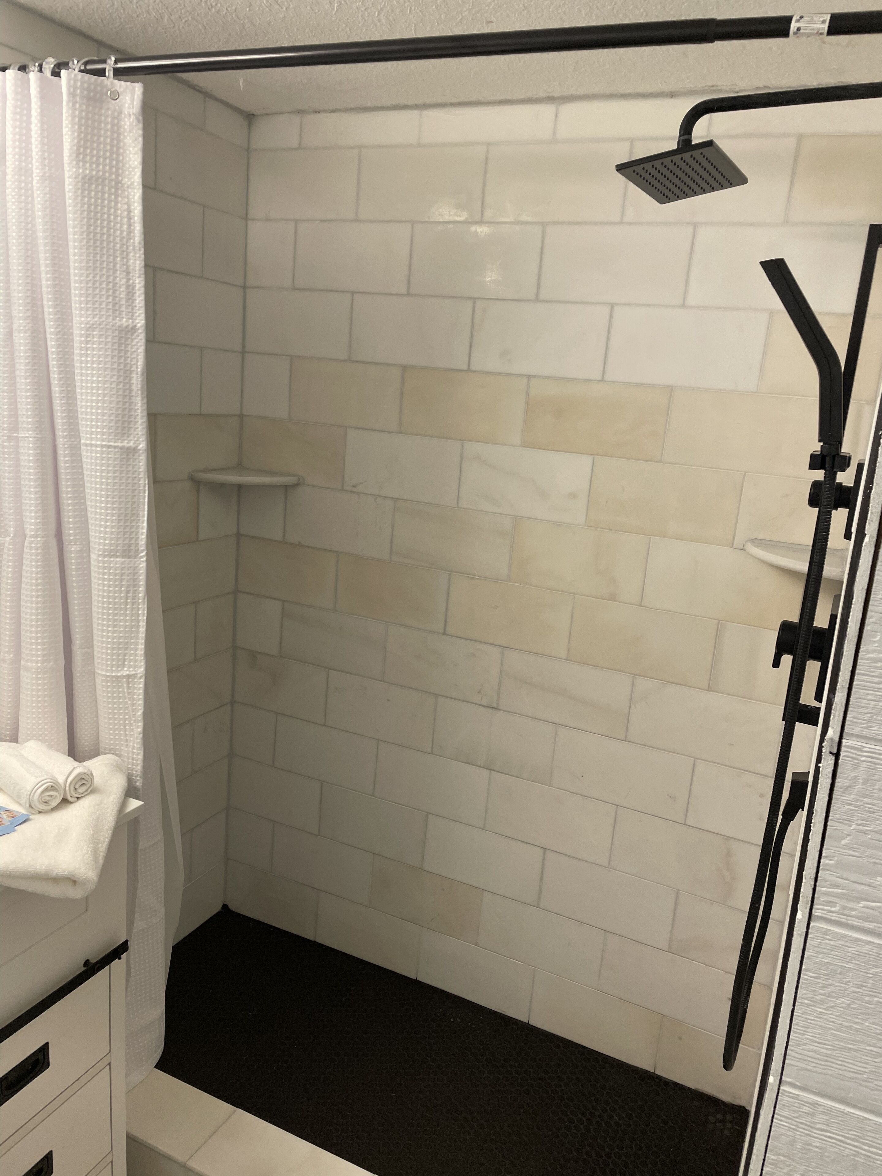 Une salle de bain avec des murs carrelés de blanc, un espace de douche noir et un porte-serviettes avec des serviettes pliées.