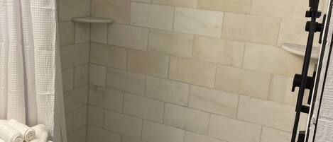 Une salle de bain avec des murs carrelés de blanc, un espace de douche noir et un porte-serviettes avec des serviettes pliées.
