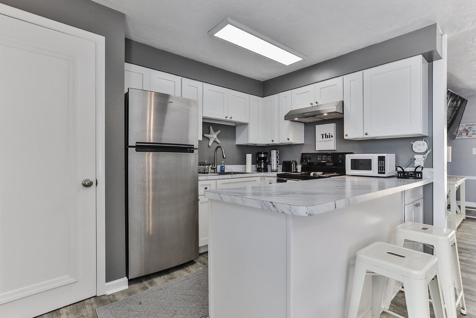 A modern kitchen with white cabinets, stainless steel appliances, and a marble countertop.