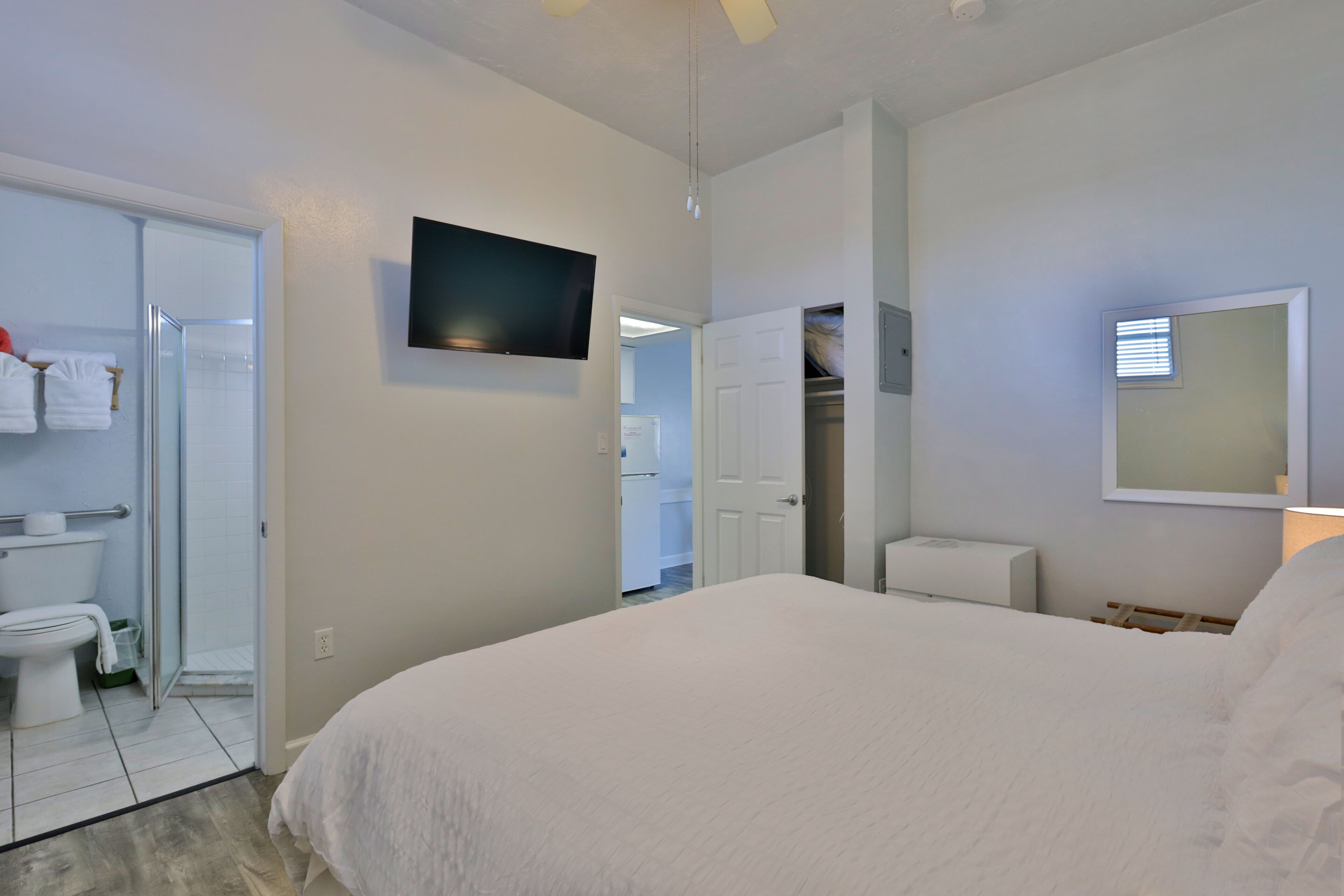 Un dormitorio con cama, televisor, armario y baño con inodoro y ducha.