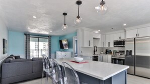 A modern kitchen with white cabinets, stainless steel appliances, and a central island with bar stools. - Coastal Waters Inn (New Smyrna Beach)