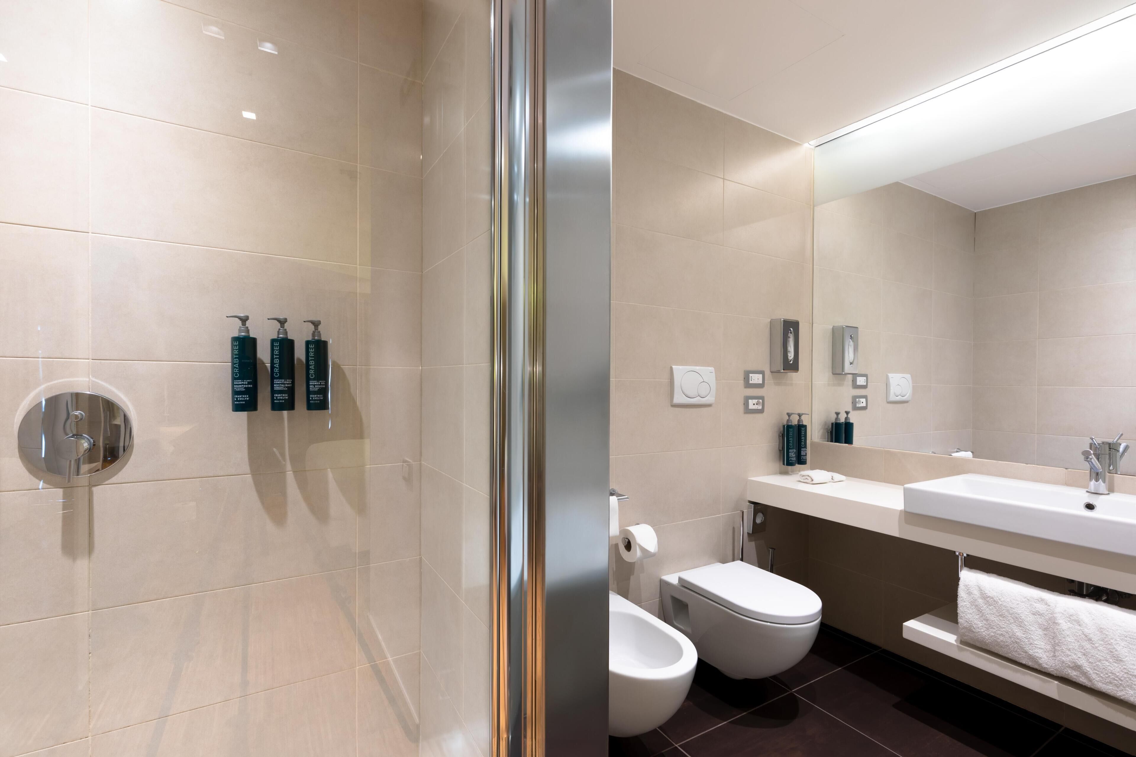 Un bagno moderno con box doccia in vetro, WC, bidet e lavandino con specchio sopra.
