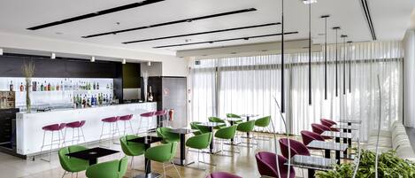 A modern restaurant with a bar area, green and purple chairs, and a wooden floor.