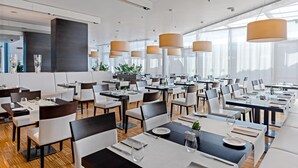 Un comedor moderno con varias mesas y sillas, ventanas amplias e iluminación colgante.
