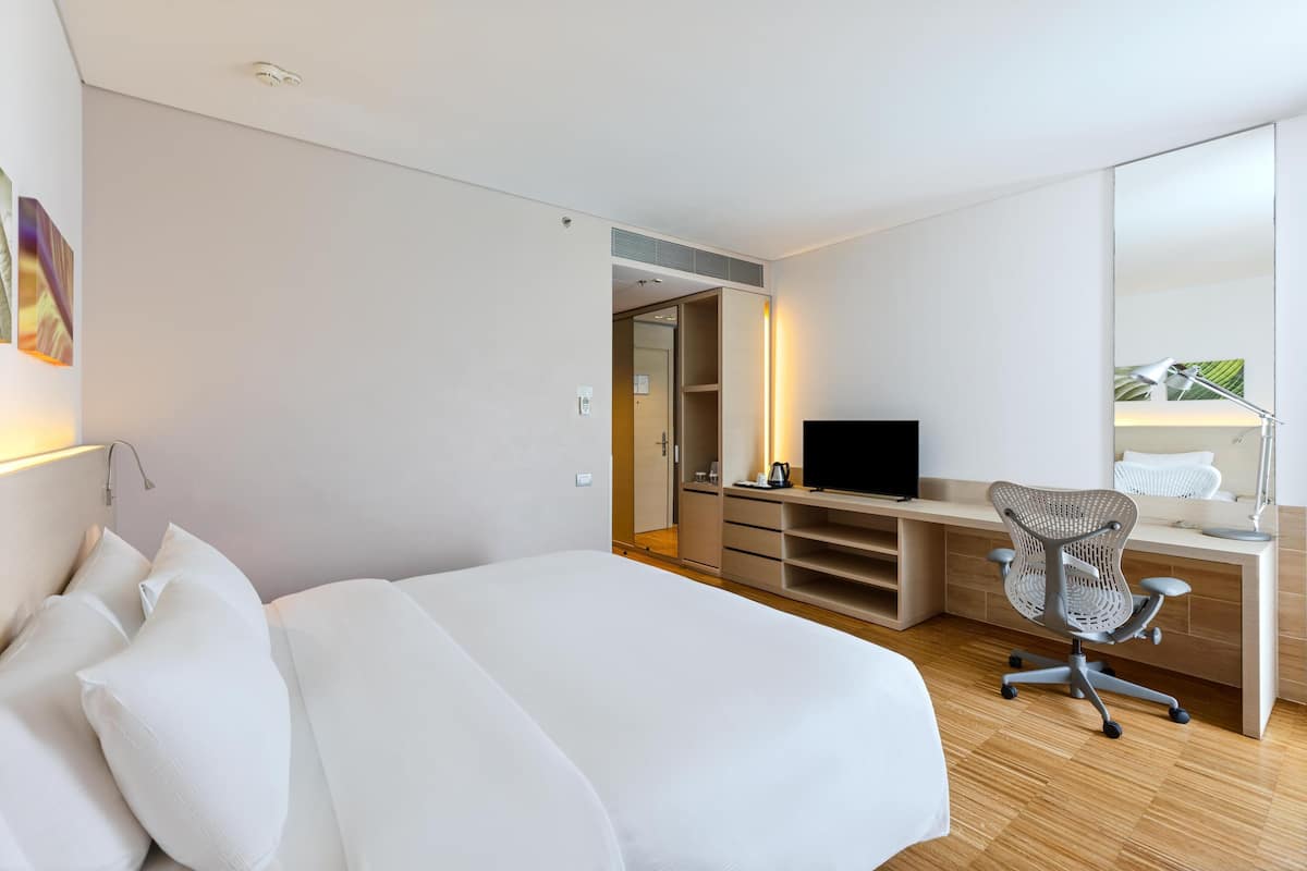 Una habitación de hotel moderna con una cama grande, un escritorio con computadora, una silla y un televisor.