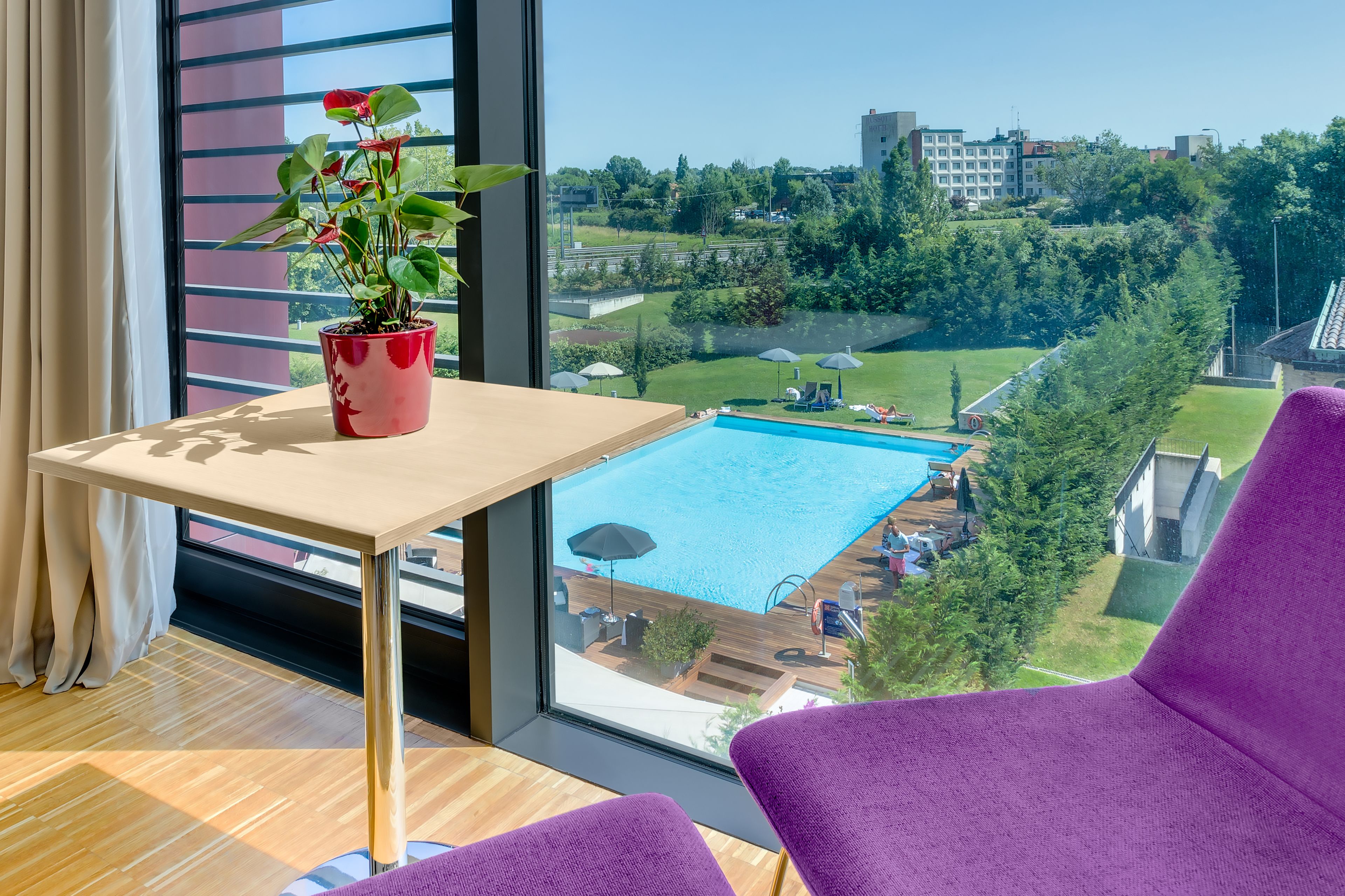 A room with a large window, a wooden table, a potted plant, and purple chairs.