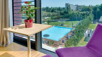 A room with a large window, a wooden table, a potted plant, and purple chairs.