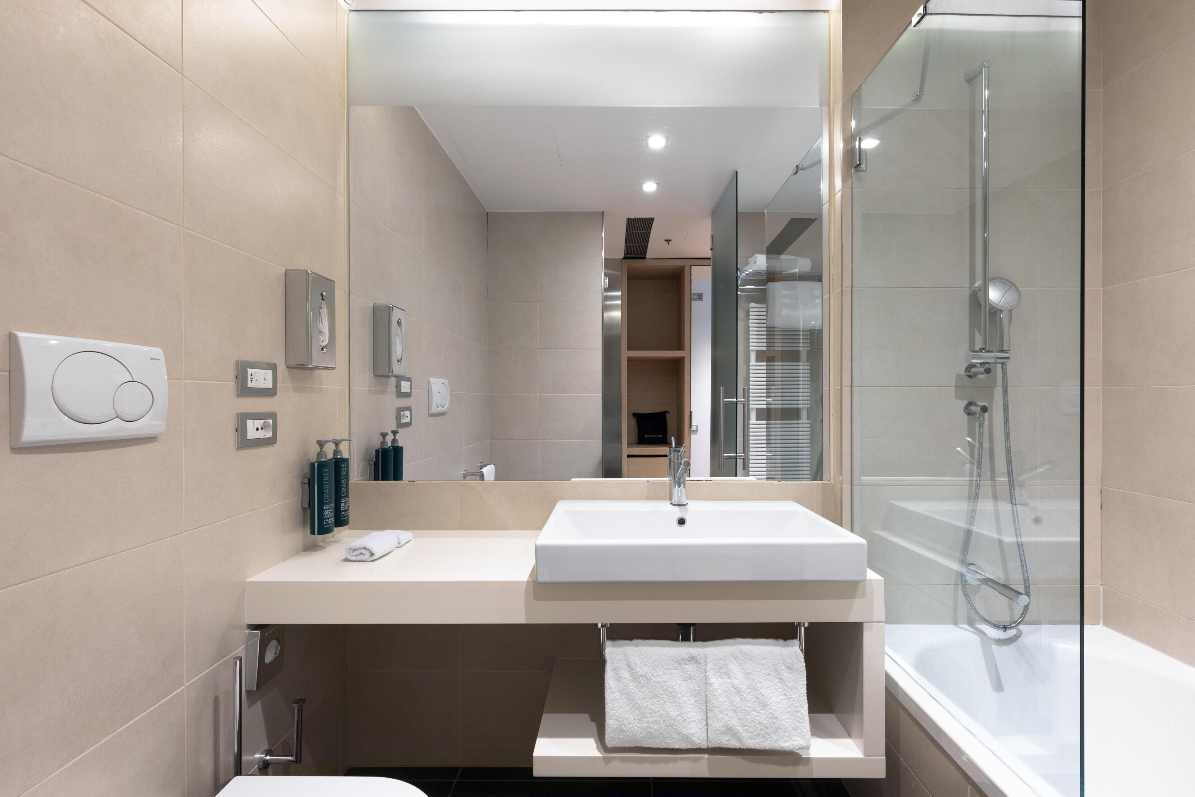 Une salle de bain moderne avec un grand miroir, un lavabo, une douche et des toilettes.
