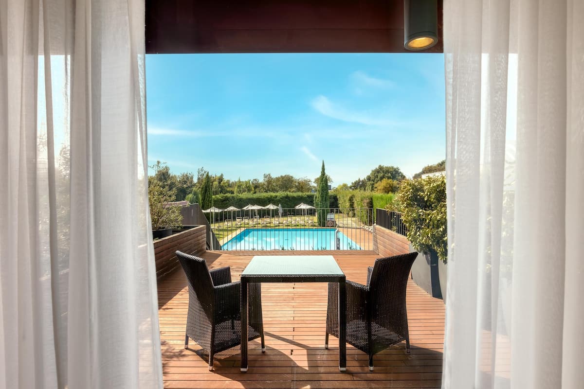 Una terraza de madera con una mesa y sillas, con vistas a una piscina y vegetación.