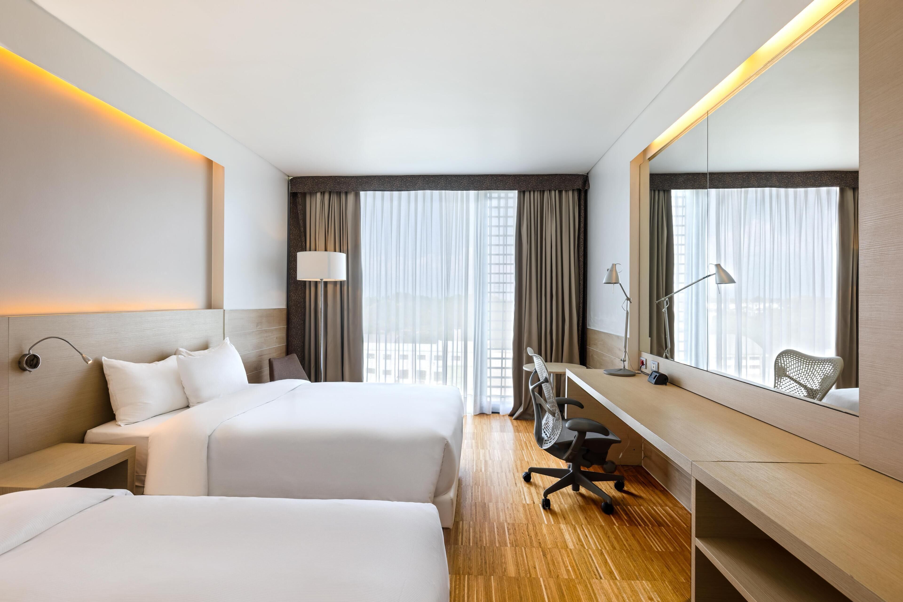Ein Hotelzimmer mit zwei Betten, einem Schreibtisch, einem Stuhl, einer Lampe und einem großen Spiegel.