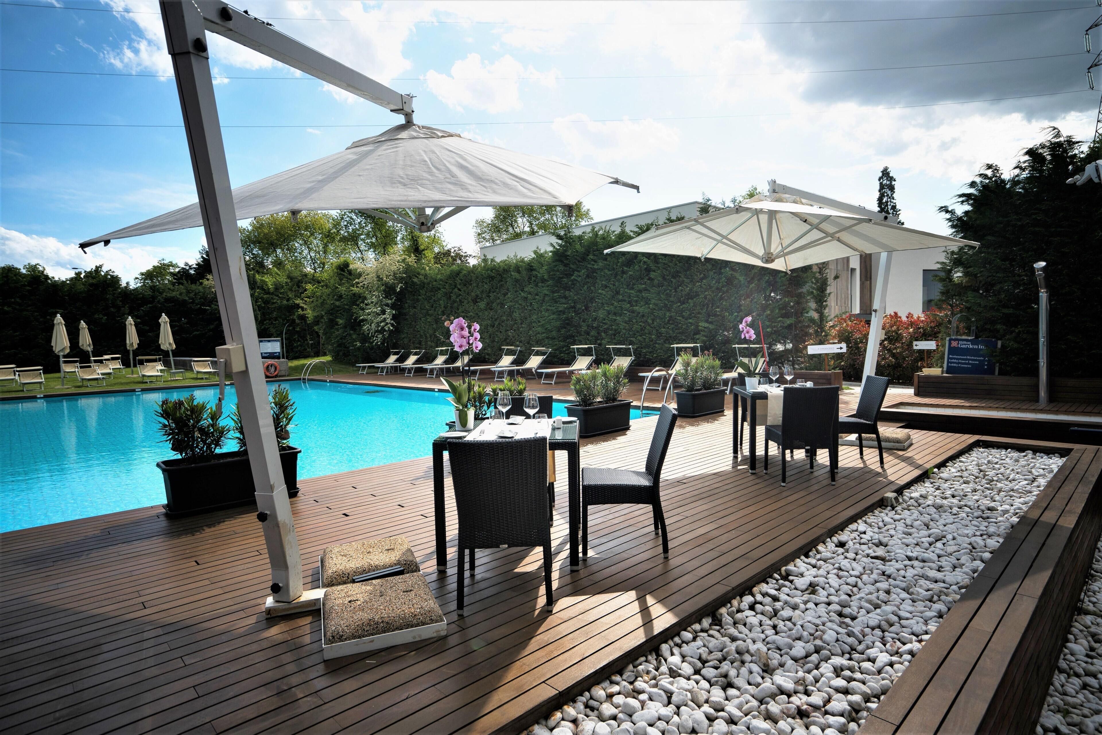 A poolside area with lounge chairs, umbrellas, and a dining setup.