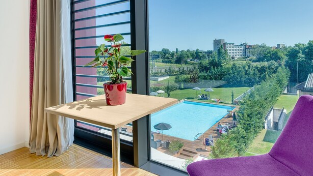 Una habitación con un ventanal amplio, una mesa pequeña con una planta en maceta y sillas moradas.
