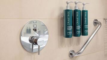 Une salle de bain avec un miroir rond, un robinet chromé et trois flacons de shampoing et d’après-shampoing de la marque Crabtree.