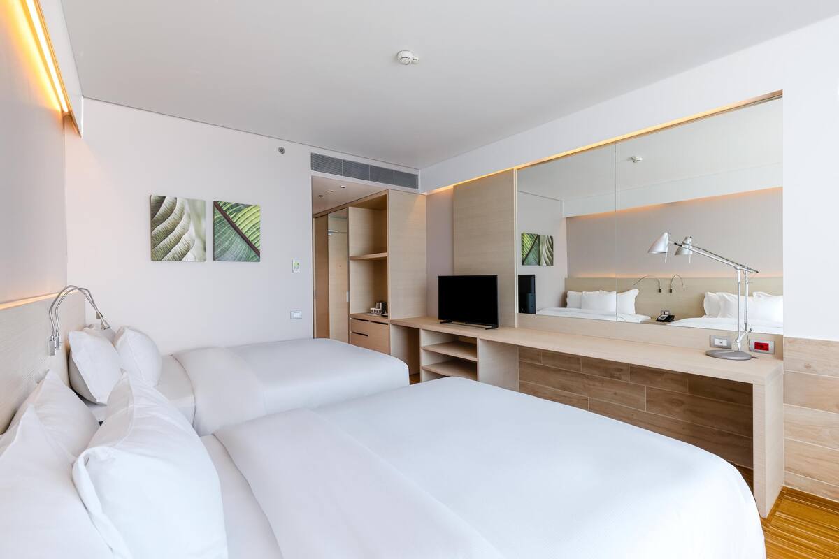 Una habitación de hotel moderna con una cama grande, un televisor, un escritorio con lámpara y un espejo.