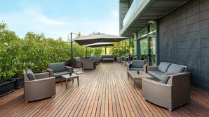 Un patio al aire libre con mobiliario de mimbre, un área de estar central y vistas a un edificio moderno.