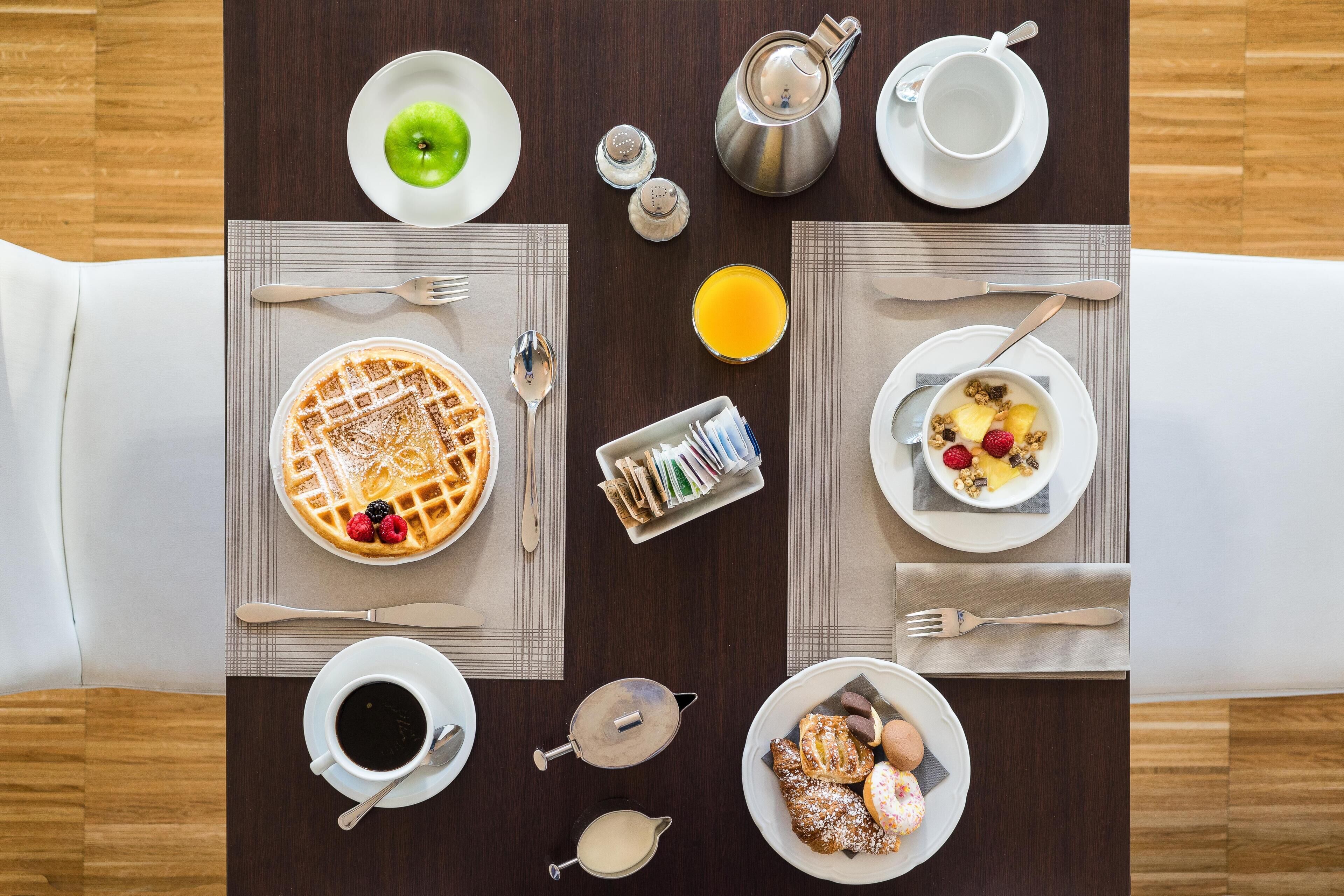 A breakfast table with waffles, fruit, coffee, and a teapot.