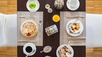 A breakfast table with waffles, fruit, coffee, and a teapot.