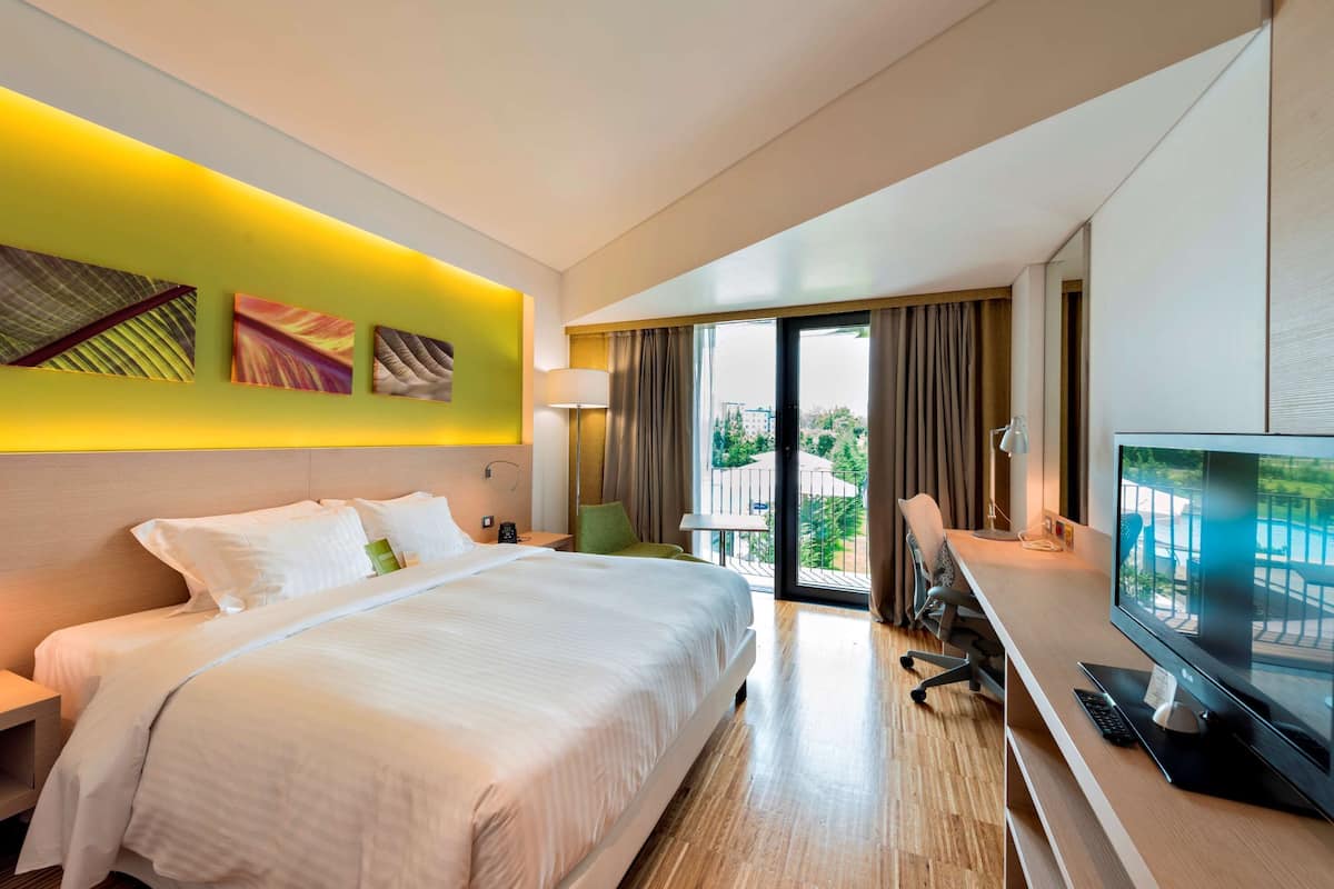 Una habitación de hotel con cama, escritorio, televisor y balcón con vistas.