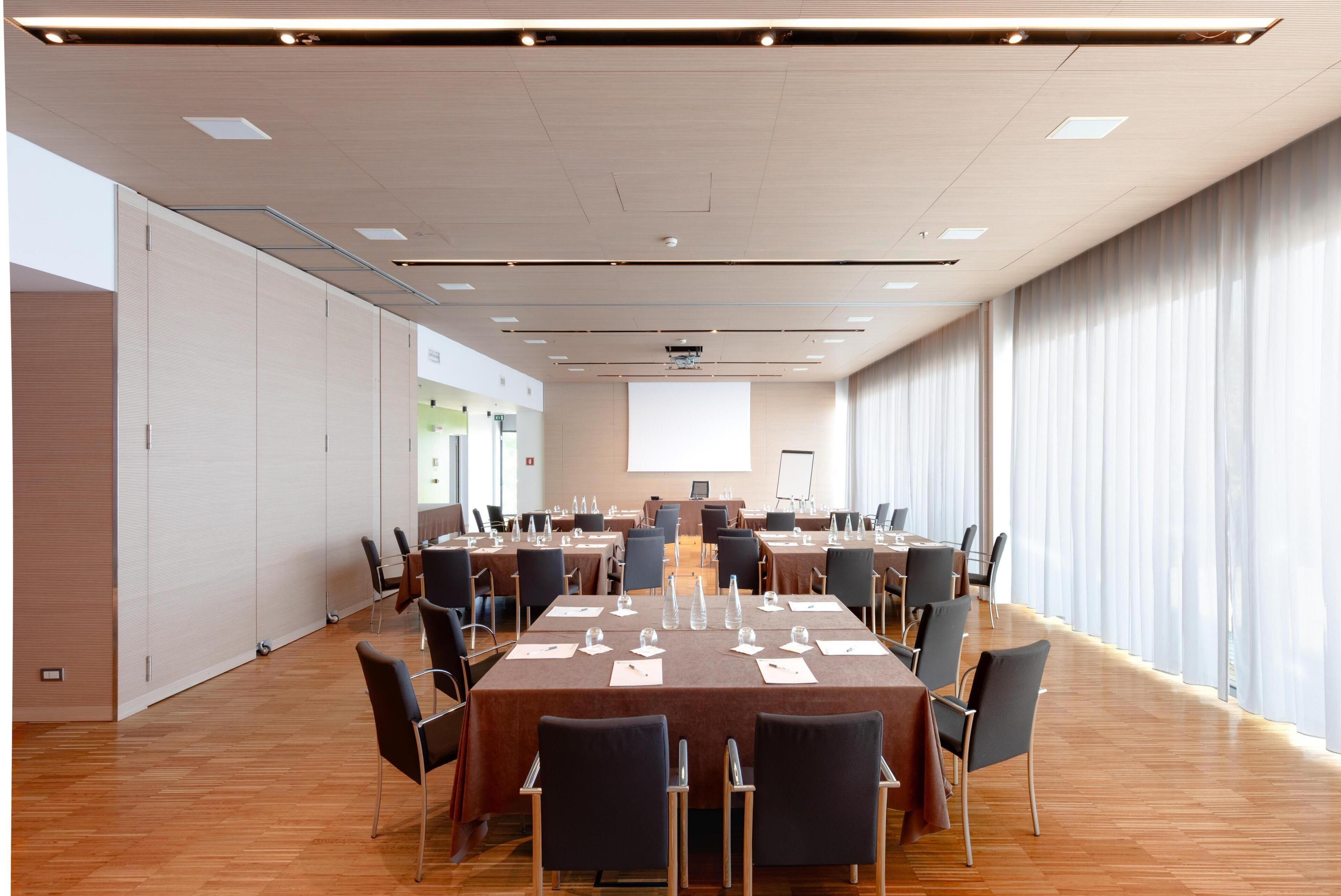 A conference room with a long table, chairs, a projector screen, and a large window.