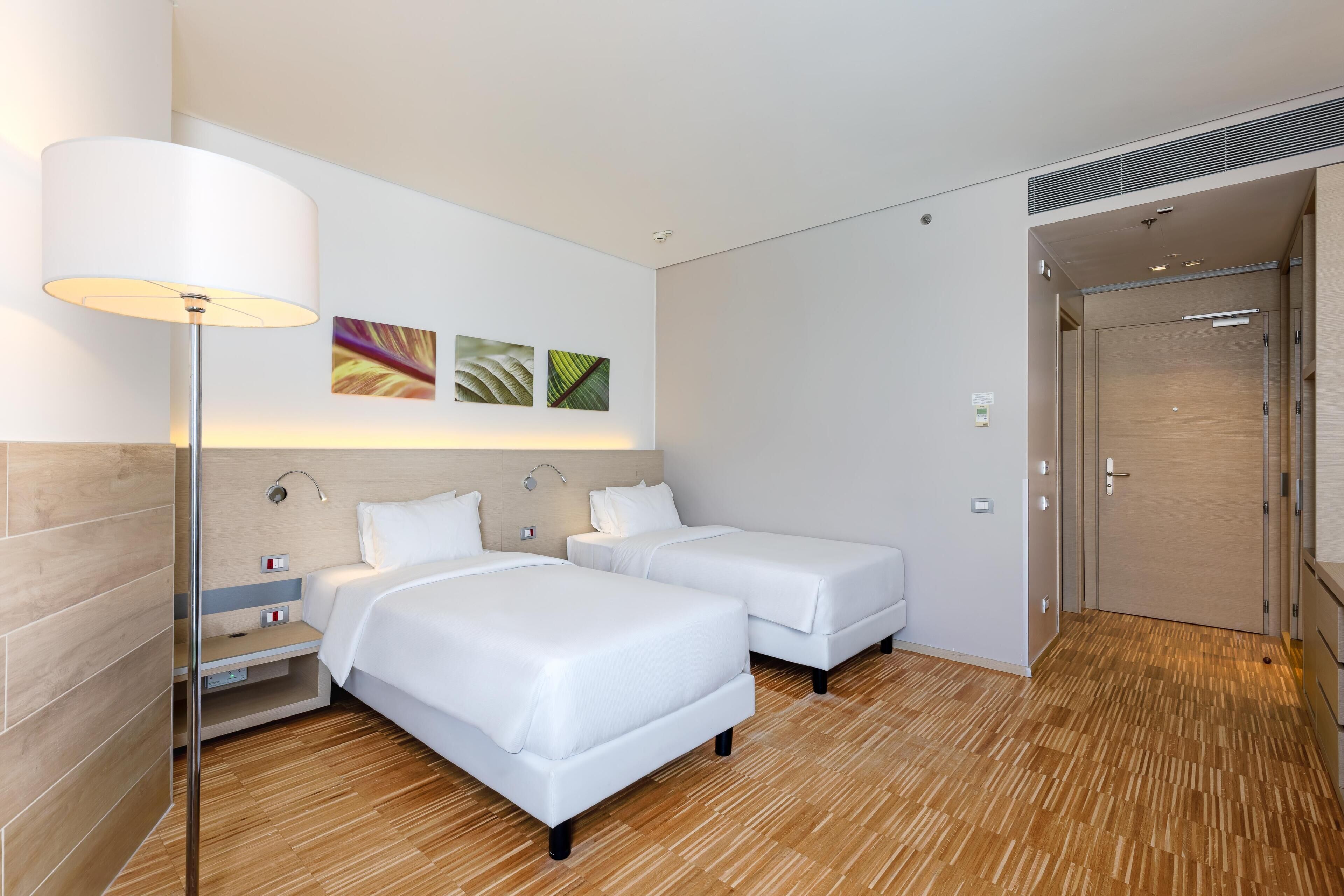 Habitación de hotel con dos camas, una mesita de noche, una lámpara y una obra de arte en la pared.