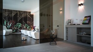 Un salón moderno con suelo de madera oscura, sofás blancos, un separador de vidrio y una pared con motivos de hojas tropicales.