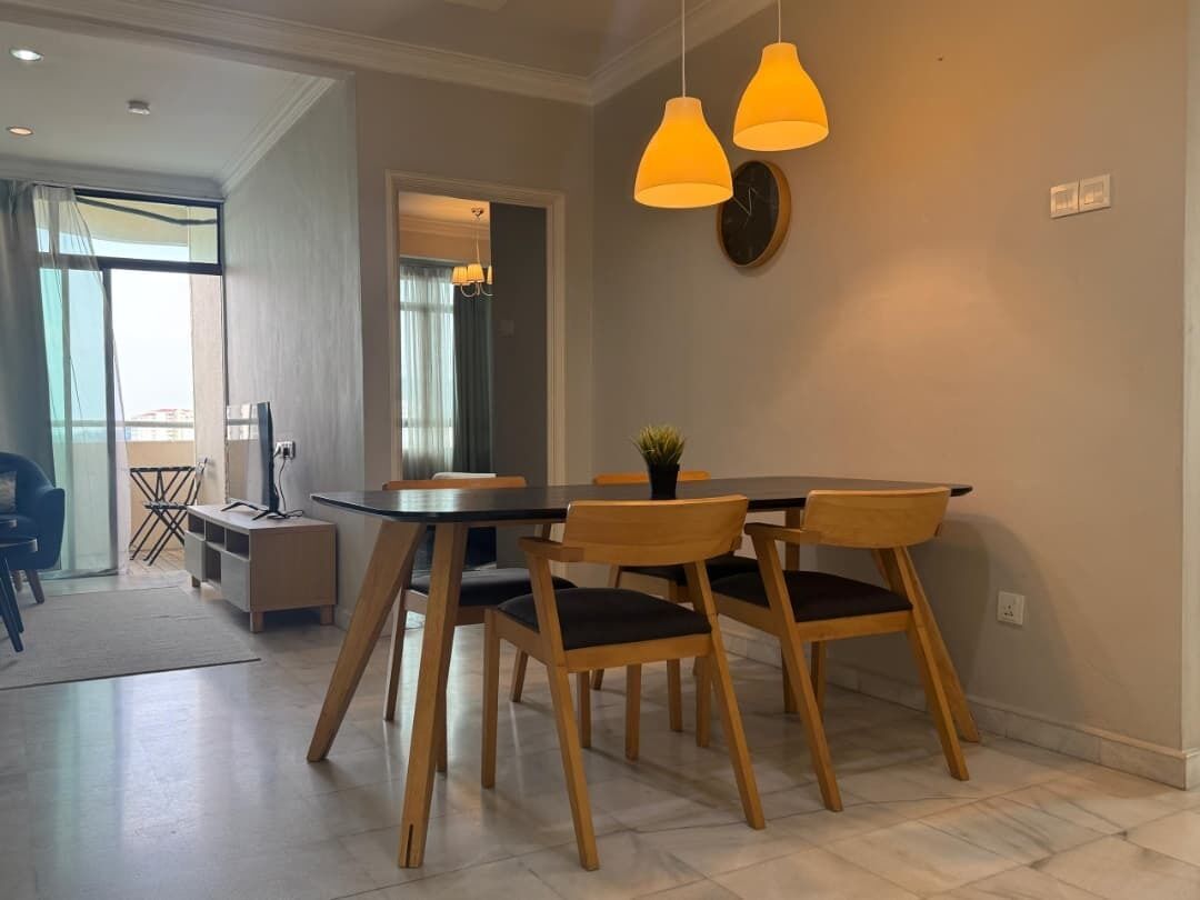 A dining area with a table and chairs, a clock on the wall, and pendant lights.
