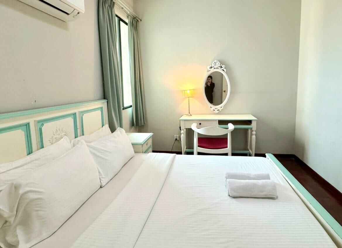 Habitación de hotel con cama, escritorio con espejo, lámpara y ventana con cortinas.