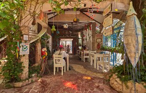 An indoor dining area with rustic stone walls, hanging decorations, and a large fish sculpture.