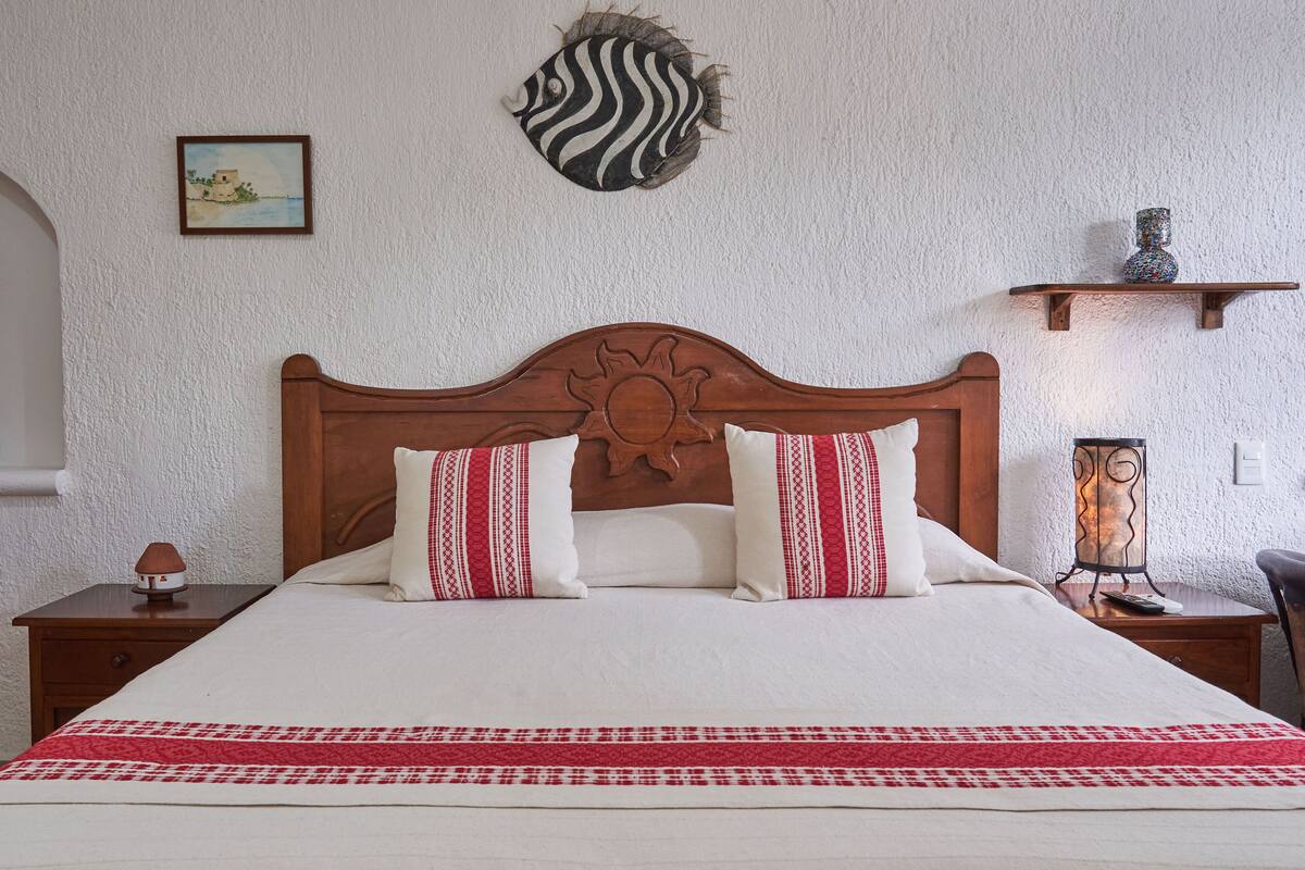 A bedroom with a wooden headboard, two pillows with red and white patterns, a white bedspread, and a red and white blanket.