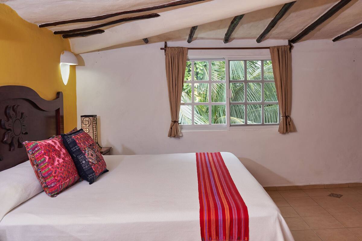 A bedroom with a bed, a window with curtains, a nightstand, and a wooden wardrobe.