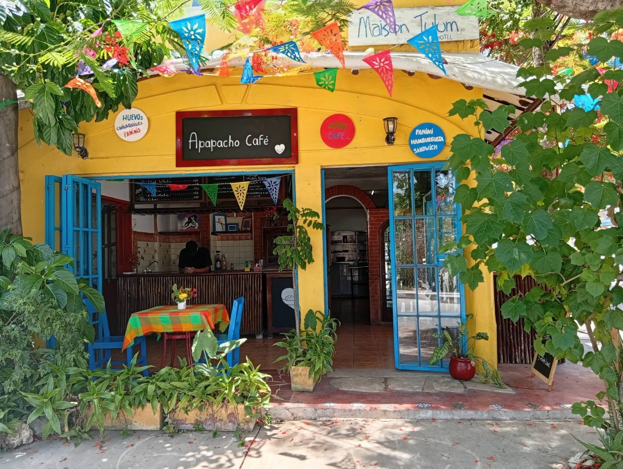 A café with a yellow exterior, blue shutters, and a sign indicating it serves Mexican cuisine.
