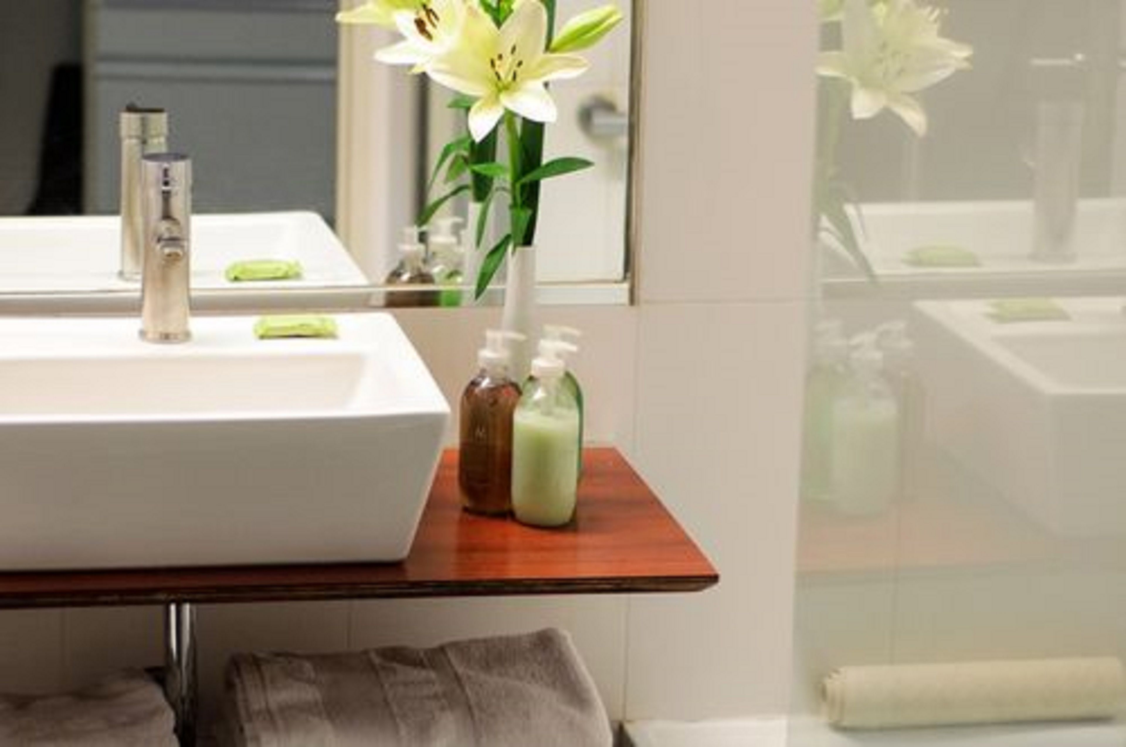 Ein Badezimmer mit einem weißen Waschbecken, einem Spiegel und Pflegeprodukten auf einem Holzregal.