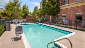 A rectangular outdoor pool with a blue edge, surrounded by a brick building, trees, and outdoor seating. - Hampton Inn & Suites Richmond/Glenside (Richmond)