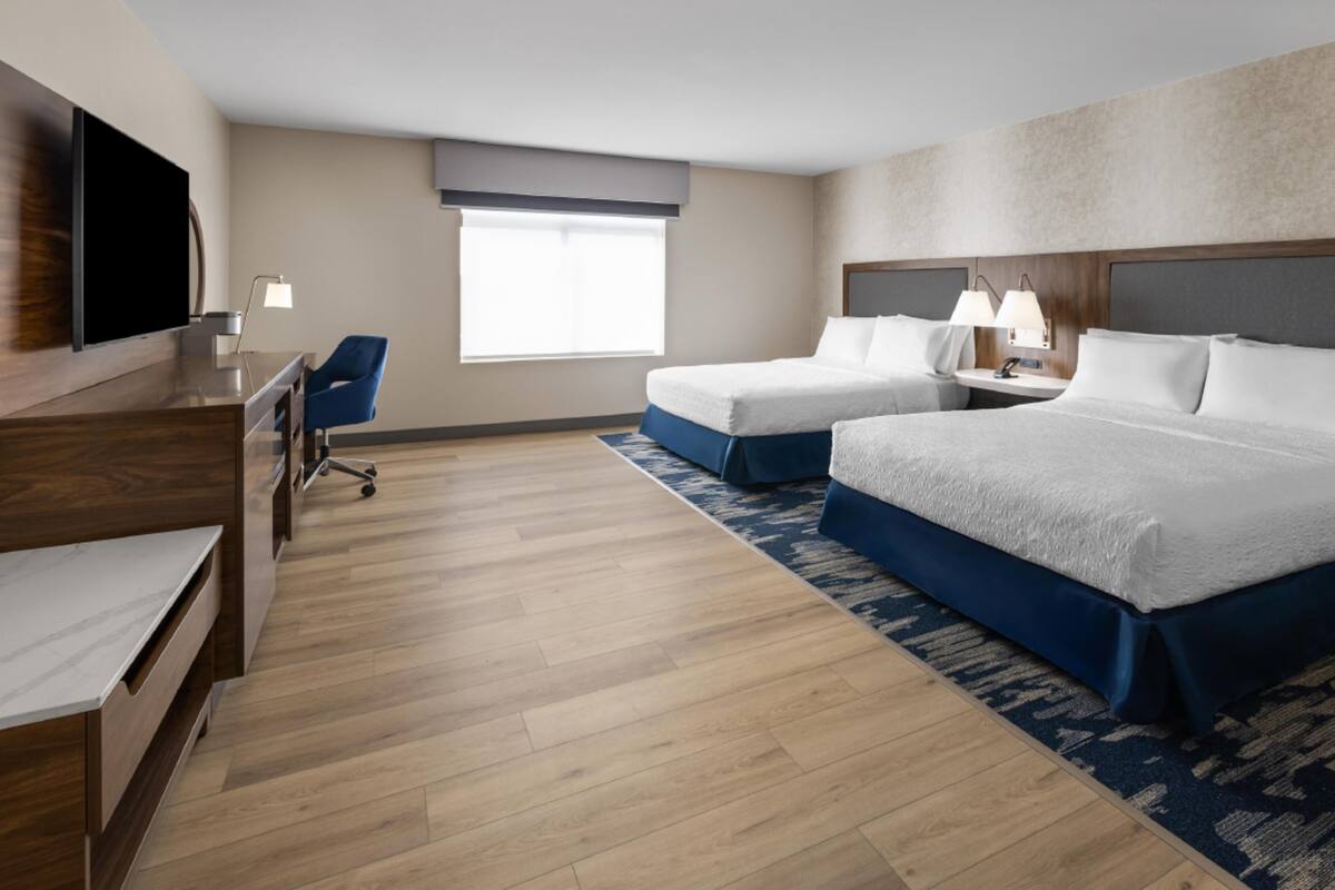 A hotel room with a flat-screen TV, a desk, two beds, a chair, and a window.