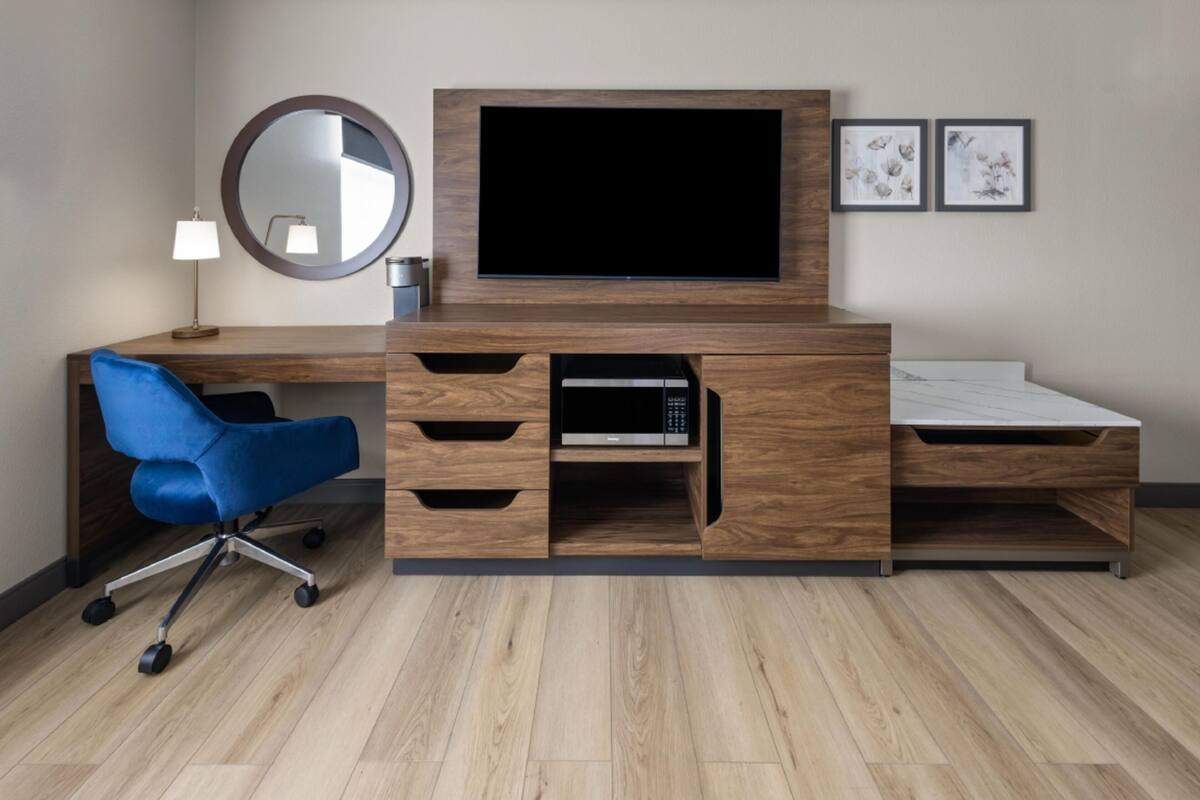 A modern bedroom with a wooden TV stand, a blue chair, and a bedside table.