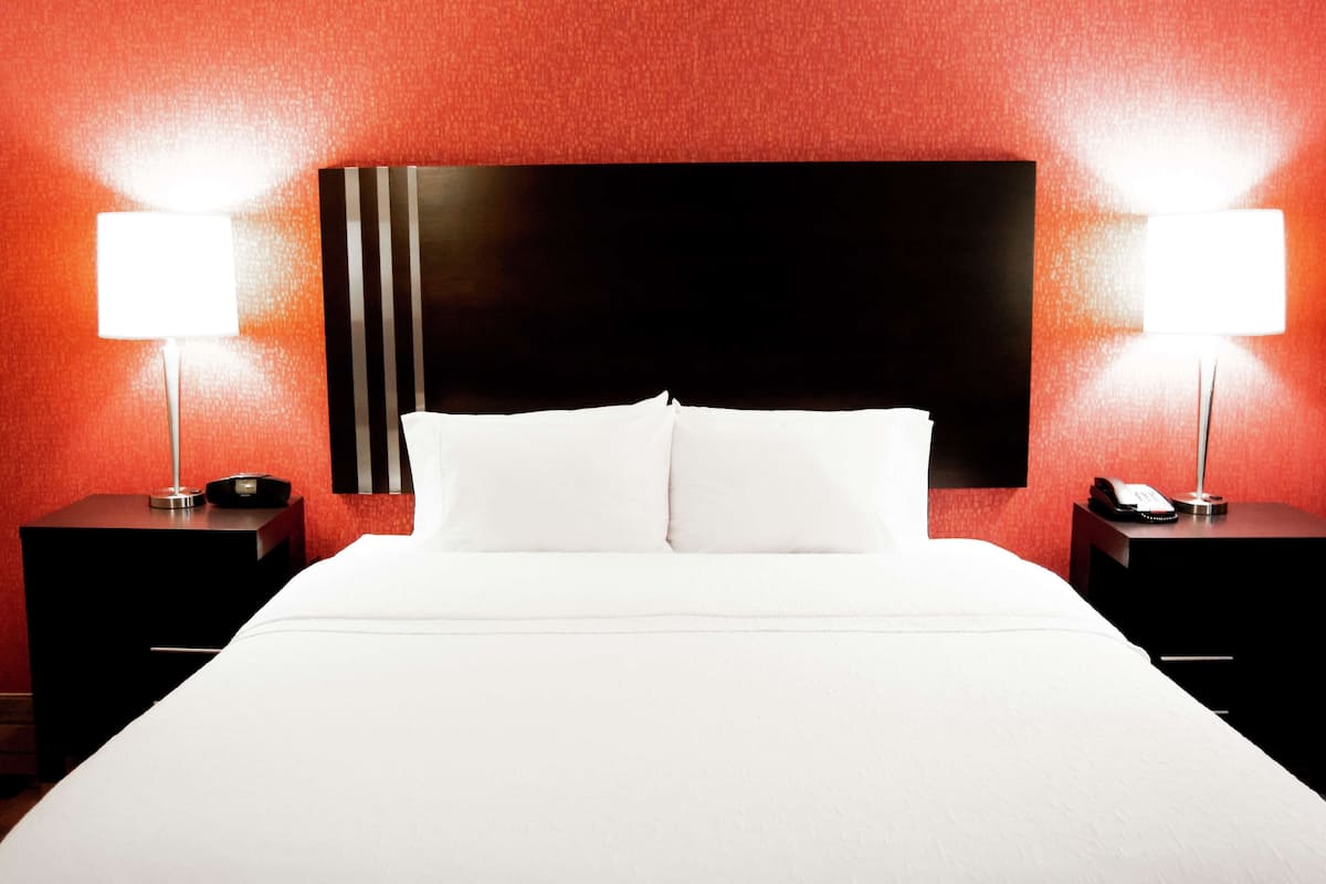 A hotel room with a large bed, two bedside tables, and two wall-mounted lamps.