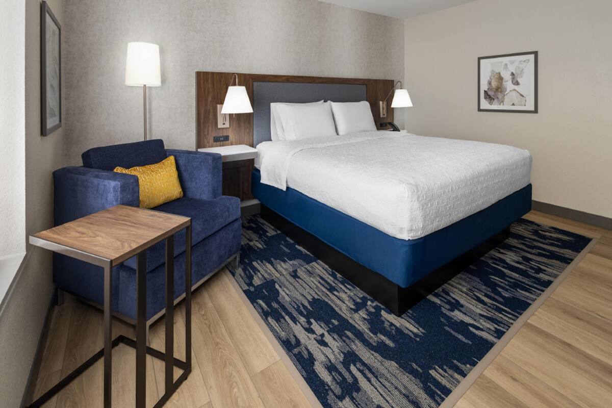 A hotel room with a bed, a sofa, a small table, and two bedside lamps.