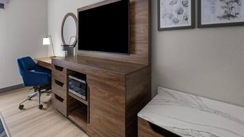 Habitació d'hotel moderna amb un moble de divinització de fusta, un televisor de pantalla plana, una cadira blava, una tauleta de nit i dos quadres amb marc a la paret.