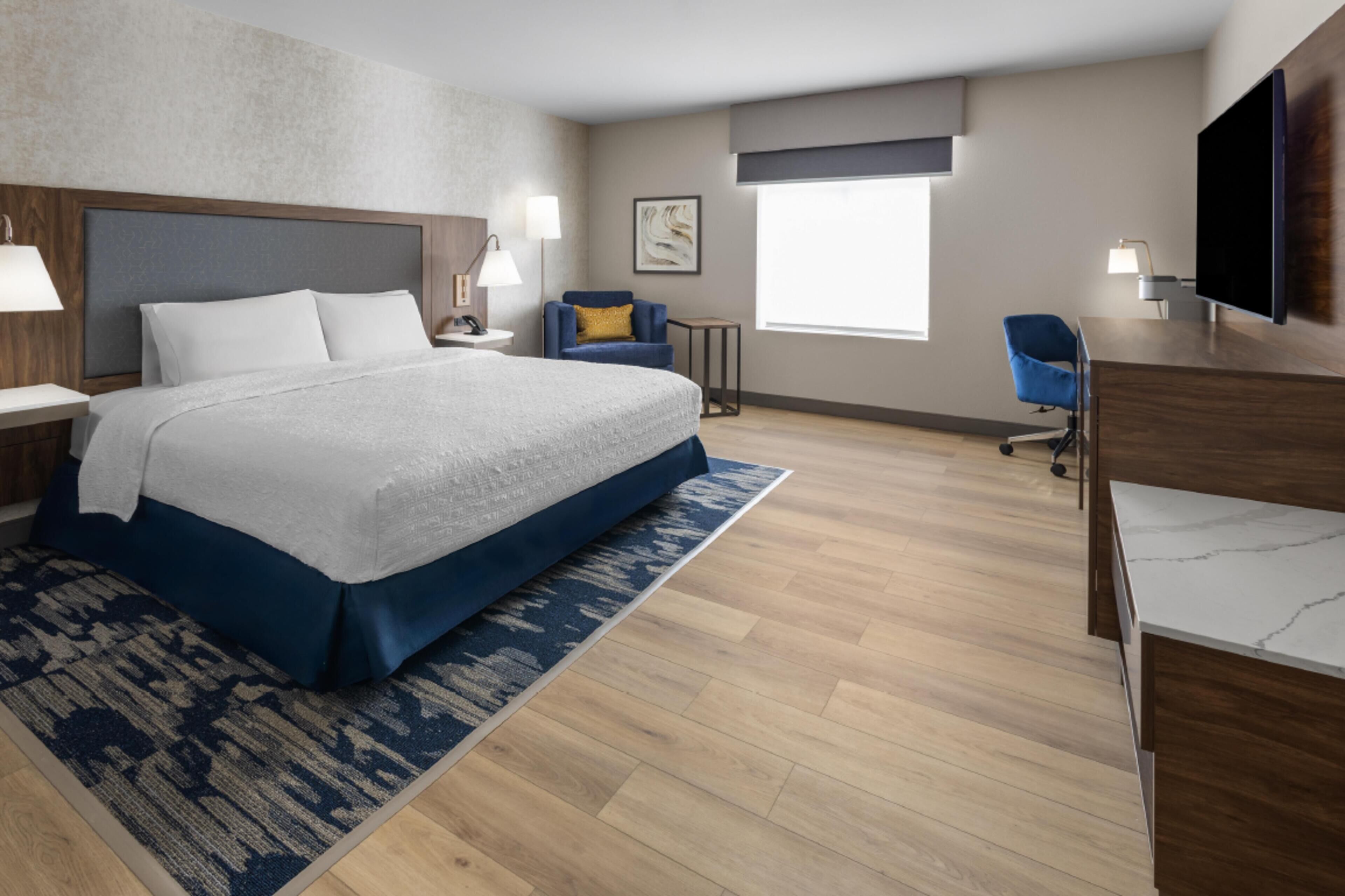 A hotel room with a large bed, a desk, a chair, a TV, and a window.