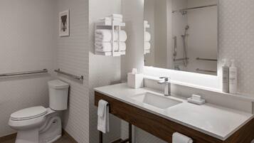 A modern bathroom with a white sink, mirror, and toilet. There are towels and toiletries on the counter.