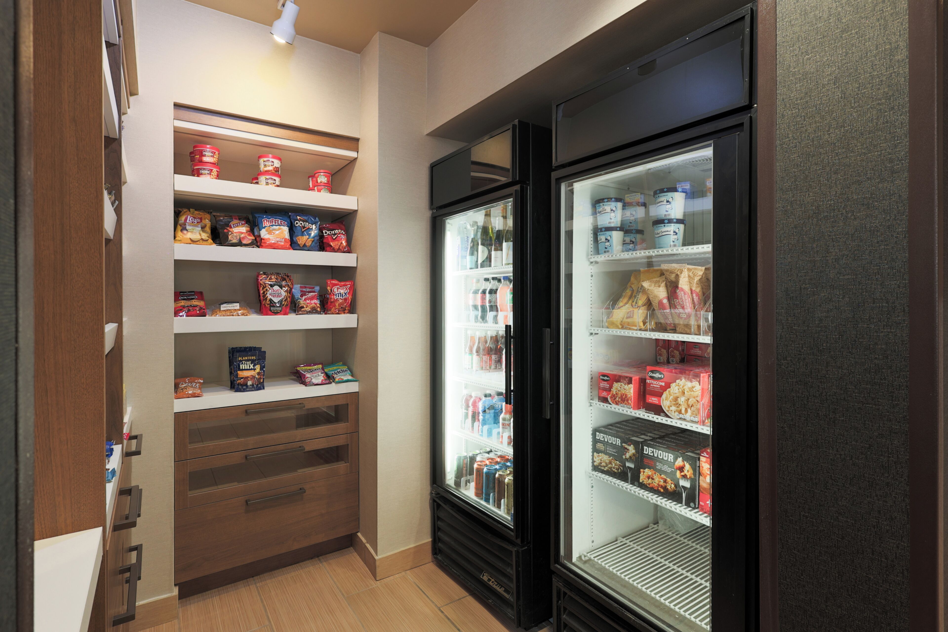 A narrow hallway with a refrigerated display case on the right and shelves stocked with snacks on the left.
